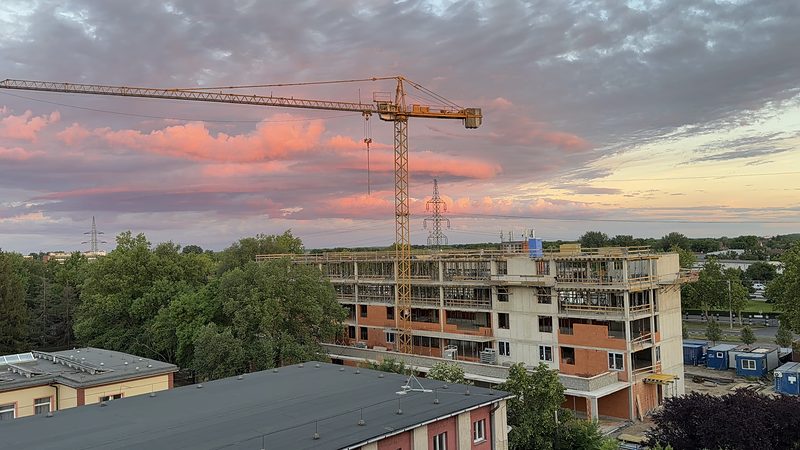 Többszintes épület szerkezetépítése toronydaruval, alkonyati égbolt alatt